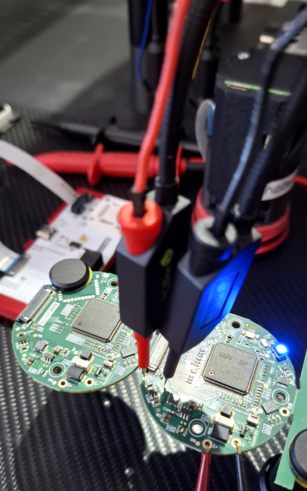 Placas eletrónicas NodeHub ligadas a sondas de teste numa bancada de desenvolvimento.